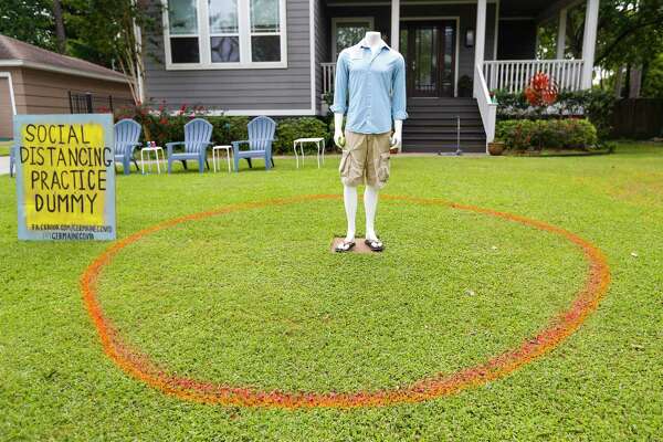 A mannequin stands inside of a circle meant to illustrate a safe distance for social distancing with a sign that reads "Social Distancing Practice Dummy" in the front yard of this home in the Timbergrove subdivision, in Houston, Monday, March 30, 2020.