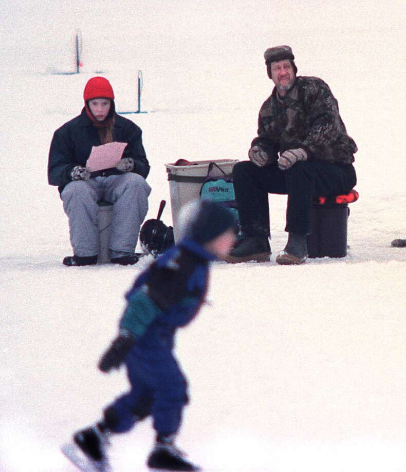 two unidentified ice fishers watch a passing skater on mill pond