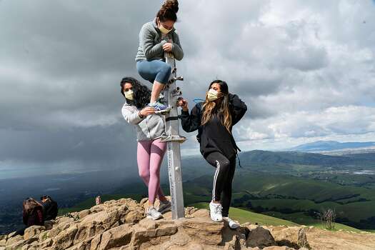 Three people, wearing protective masks, get set up for a photo at Mission Peak on Thursday, March 26, 2020, in Fremont, California.