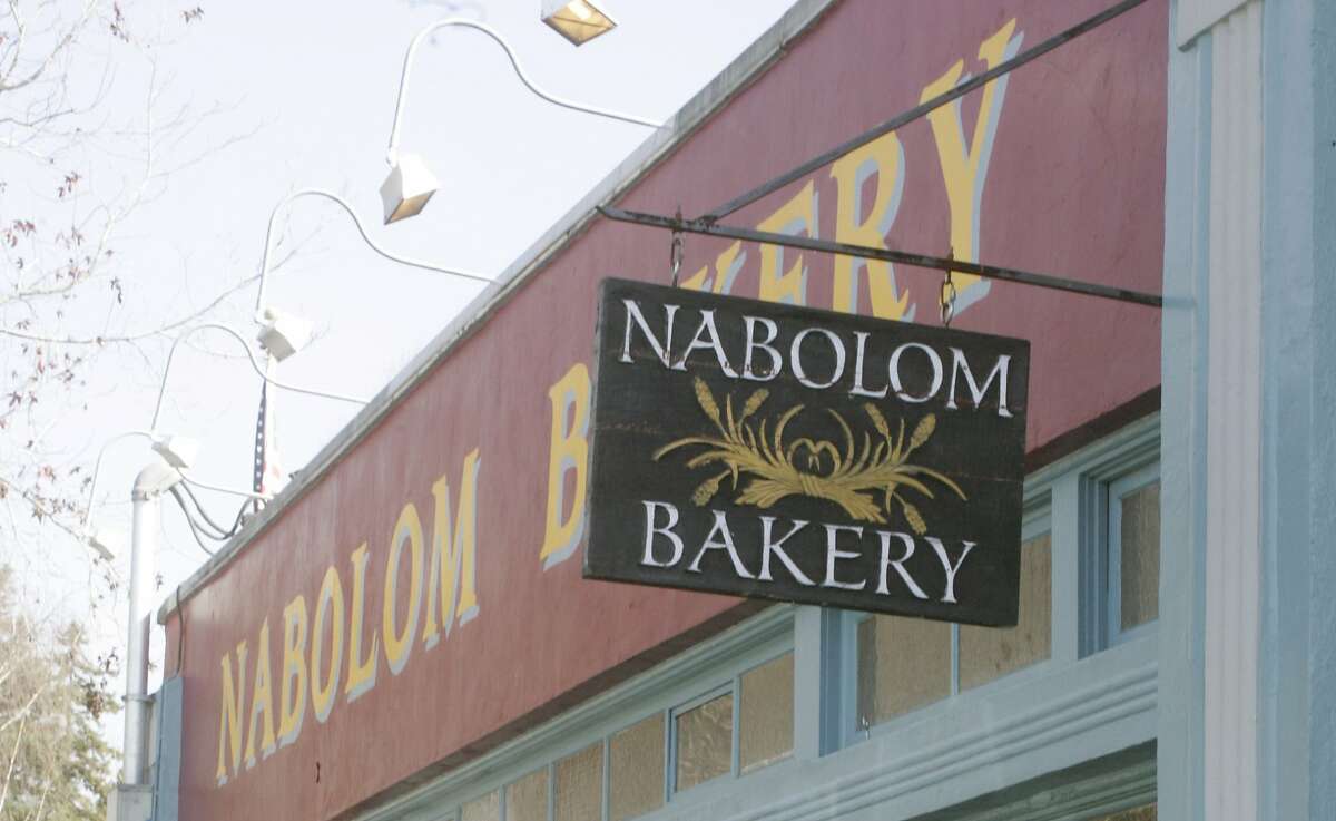 Nabolom Bakery's wooden sign and logo, in front of a red building with the yellow Nabolom Bakery font.