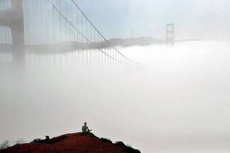 A man sitting on a hill with the Golden Gate Bridge in the background