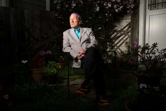 A portrait of Tom Ammiano in his backyard. He is wearing a gray suit jacket and a teal shirt.