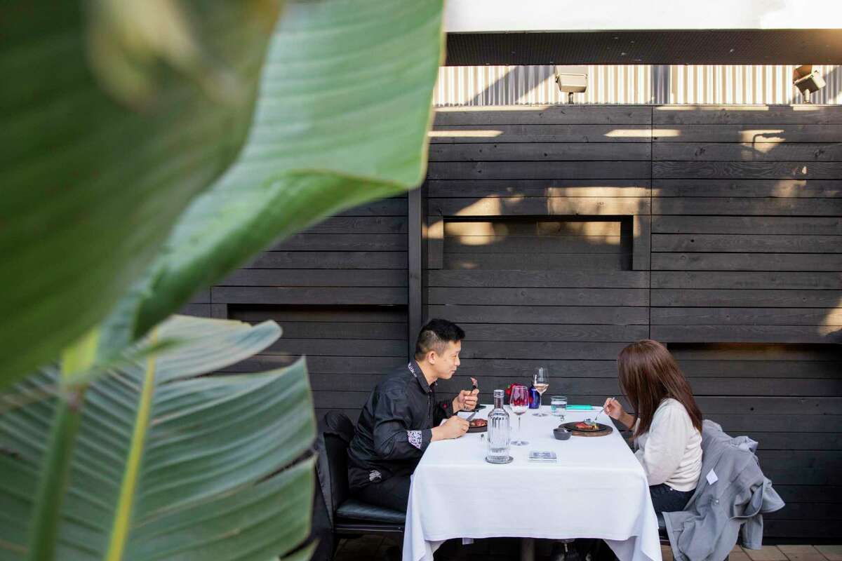 A man and a woman dine on the patio at Californios next to a large green plant.