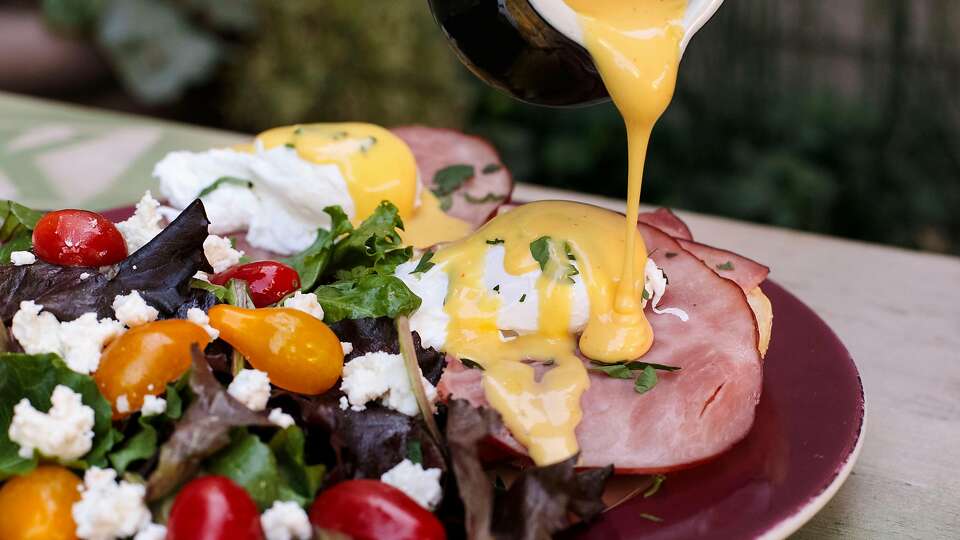 Hollandaise being poured onto eggs benedict.