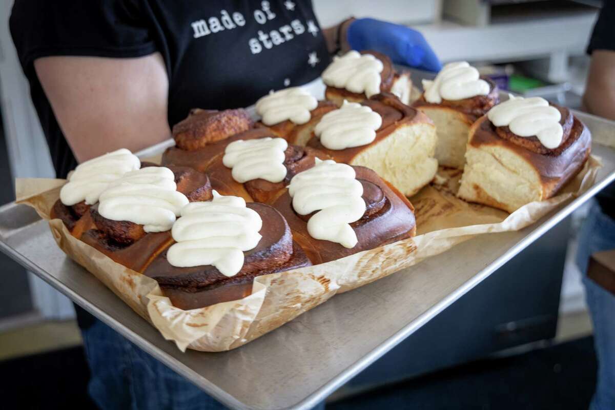 a person holds a tray full of cinnamon rolls covered in icing