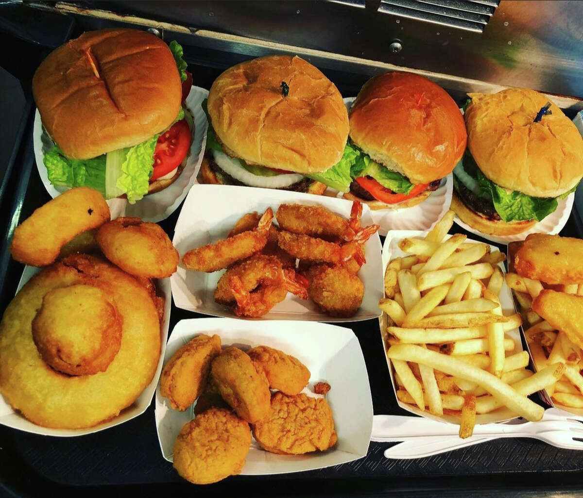 An overhead view of many types of road food in paper trays., including four types of burgers, onion rings, chucken nuggets, and french fries.