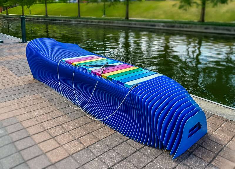 A blue bench with a xylophone in the middle. Located in The Woodlands, Texas.