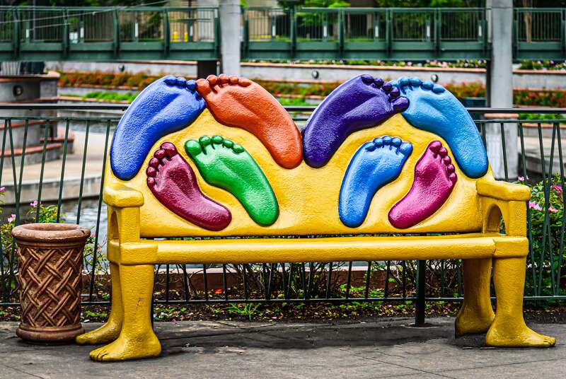 A bench with foot prints in colors of blue, orange, green and purple. Located in The Woodlands, Texas.