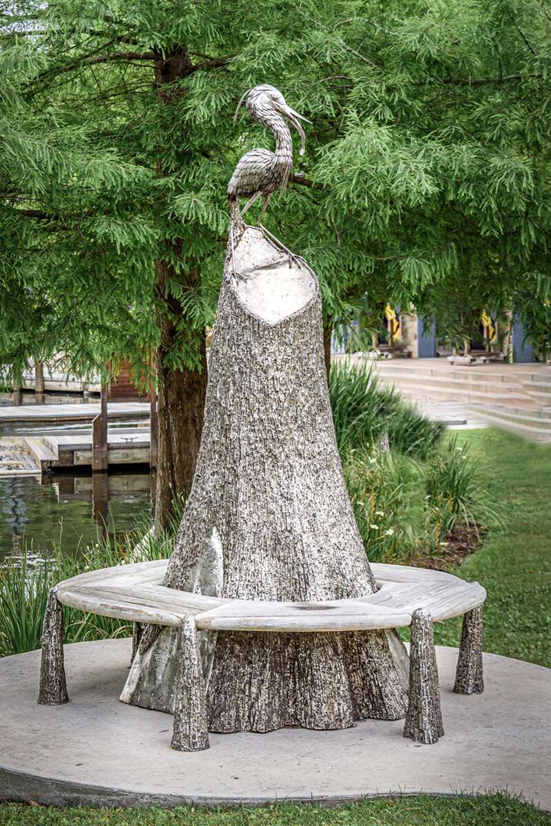 A bench with a tree stump in the middle and a bird on top. Located in The Woodlands, Texas.