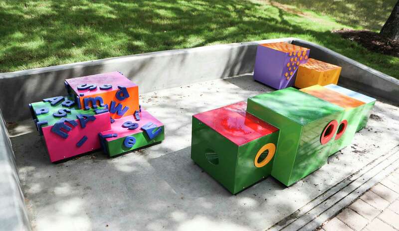 Three seperate benches in the shapes of cubes, colored green, pink and orange.