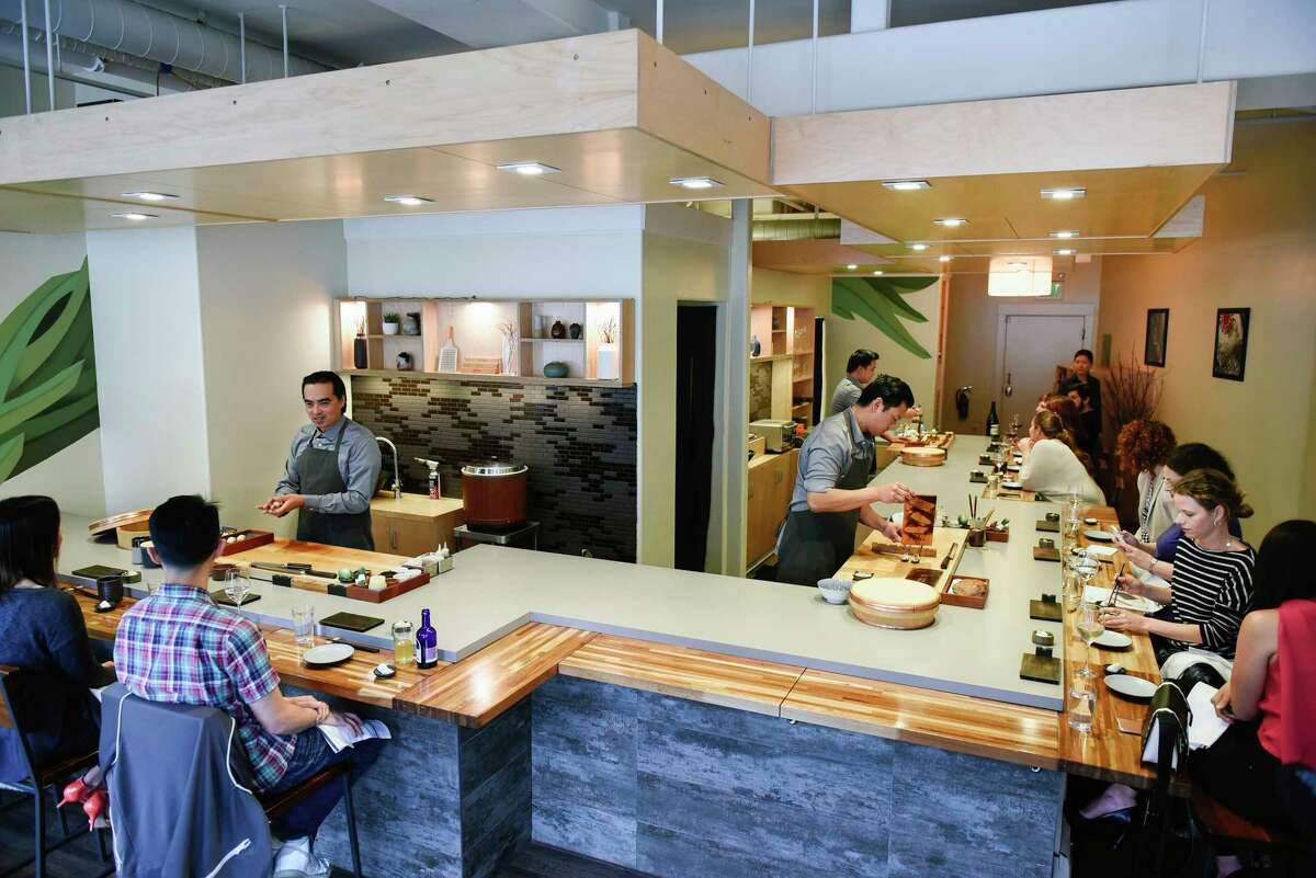 Three chefs make sushi behind a counter full of diners.