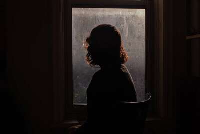 A woman with back turned is silhouetted by a window.