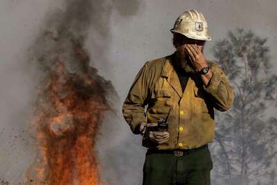 A firefighter rubs his face as a smoke-filled sky fills the background.