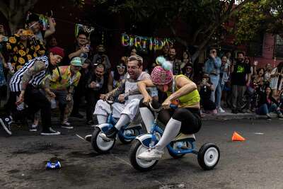 Cesar Valdivia and Gina Lomeli ride tricycles on a San Francisco street as a crowd cheers them on.