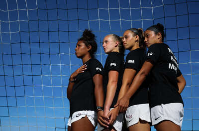 Four college-age female soccer players stand in a row.
