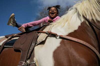 Deja Leslie, 7, smiles in delight as she mounts a horse. 