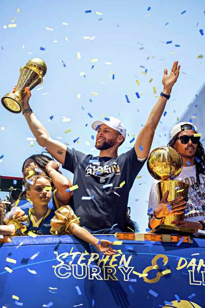 Steph Curry raises his arms in triumph as he stands with his family on a bus in San Francisco.