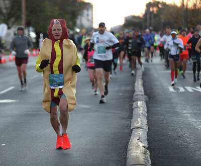 A man runs down a crowded street wearing a hot dog costume.