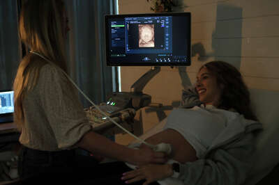 A woman receiving an ultrasound smiles as the image appears on a screen near her head