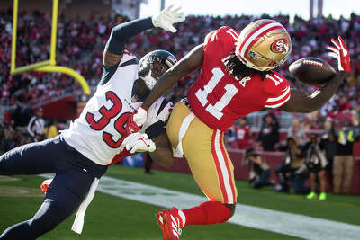 SF player reaches for a thrown football beyond the graps of Texans player in the end zone.