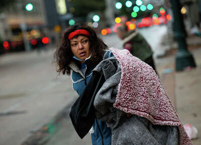 On what looks to be a cold, gray morning, a woman looks back over her shoulder as she carries several thick blankets.