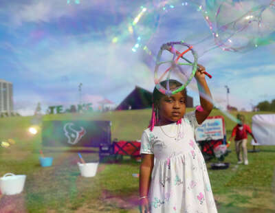A young girl's gaze sets on the camera as she fills the cameras frame with a giant bubble where she plays on a grassy field.