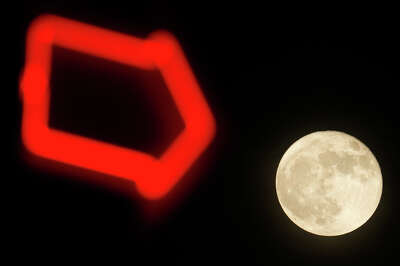 An image of the moon is juxtoposed with a red, neon sign in the foreground.