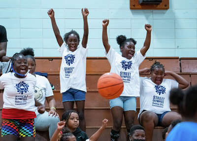 Children cheer from the bleachers as a basketball falls down in the foreground 