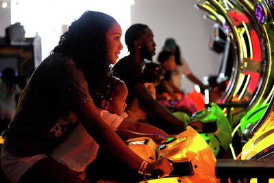 A teenager shares a videogame motorcycle with a small girl as the light from the game lights up their faces.