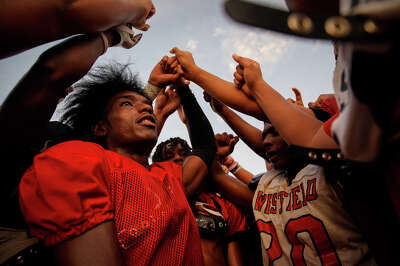 High school football players are seen from the inside of a circle of the players putting their arms into the air for a cheer.