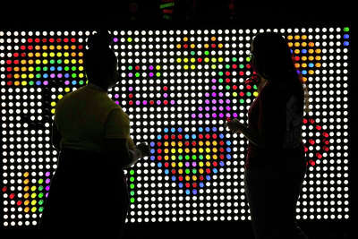 Two women are silhoutted against a wall of multi-colored lights