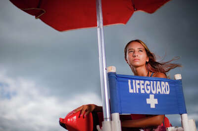 A girl looks back into a light where she sits in a lifeguard chair on a beach