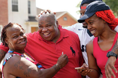 A man smiles as he is surrounded by smiling family members embracing him, one with a hand on his head