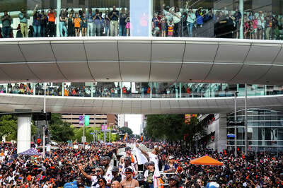 People fill a skybridge that goes over the street, as people fill the street below where a float holding astros players rolls through downtown.