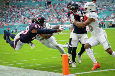 A player leaps and is suspended in mid air stretching their arm out with the football towards the end zone pylon as an opposing player tries to knock them out of bounds.