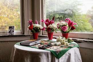 A table is set with an altar comprised of a white table cloth, a notebook and flowers near a window.