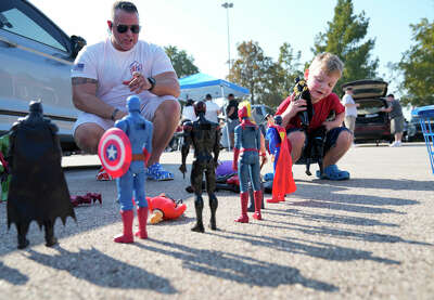 A young boy lines up super hero action figures, casting their shadows onto the parking lot ground, as his dad crouches down to watch.