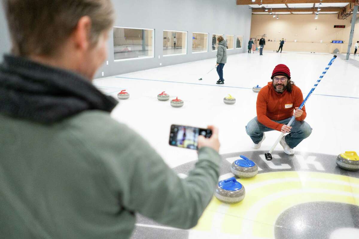 A student takes a photo of an instructor who is on the ice and explaining the sport of curling
