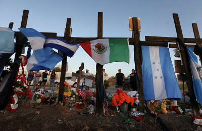 Wooden crosses adorned with flags from Mexico, Guatemala and Honduras placed at a memorial for the 53 migrants who perished in the back of a commercial trailer truck.