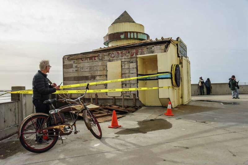 Jim Macaire stands near a bicycle in front of the damaged Camera Obscura, which is partly cordoned off by yellow "caution" tape.