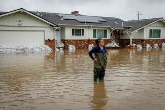 Colleen Kumada-McGowan stands in flood waters in front of her home in a neighborhood off of Holohan Road near Watsonville, Calif.