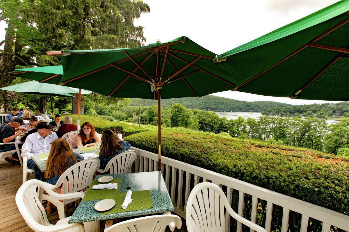 People eat outside at tables underneath canopies. A river and hills are visible in the near distance.