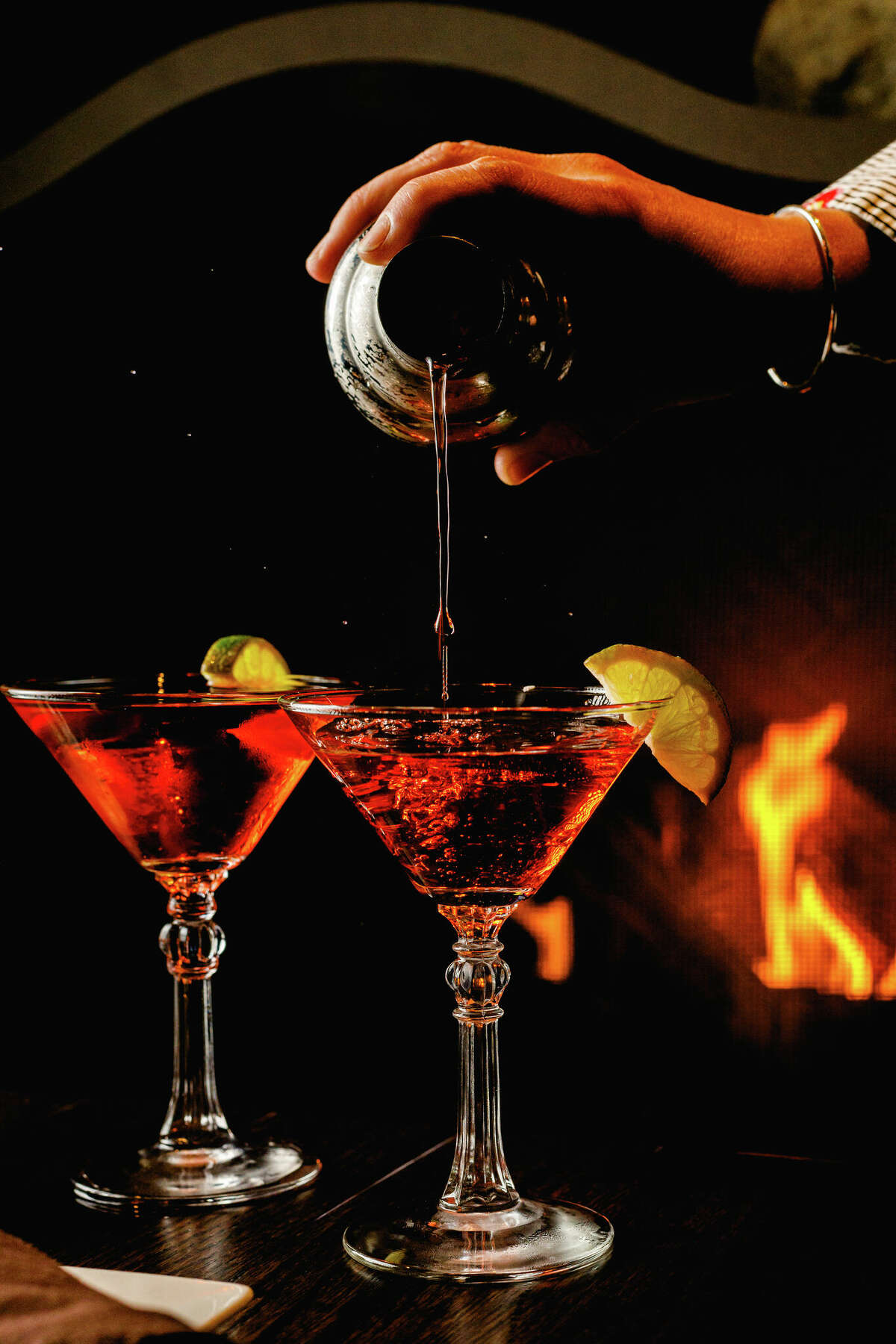 Two martini glasses being poured in front of a roaring fire