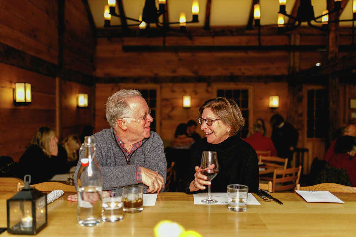 An older couple sitting at a bar in a warmly lit room, smiling and enjoying each other's company