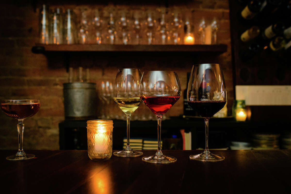 three glasses of wine sit atop the counter at a bar