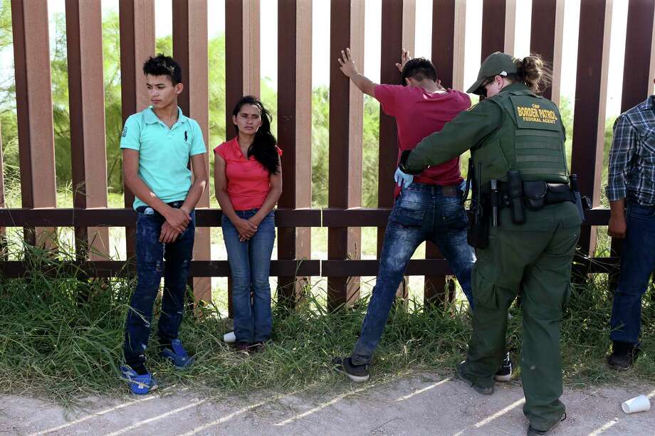 A group of immigrants turned themselves over to the Border Patrol and requested asylum after crossing the Rio Grande illegally. Santos Able Madrigez, 34, and her son, Nelson Ortez, 17, wait as agent Amber Peterson pats down an immigrant at the border fence in Hidalgo. Photo: JERRY LARA, San Antonio Express-News / San Antonio Express-News