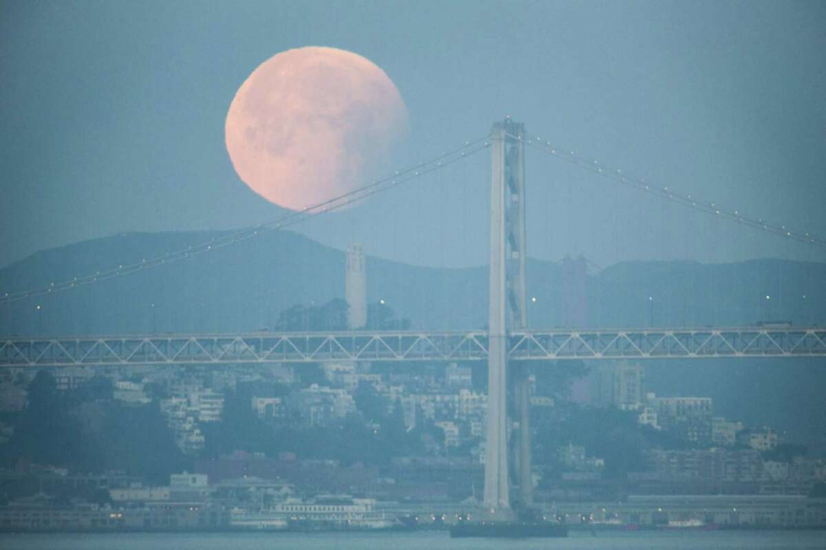 A rare super blue blood moon sets behind the Bay Bridge last January. The lunar eclipse on Sunday is likely to be obscured by clouds.