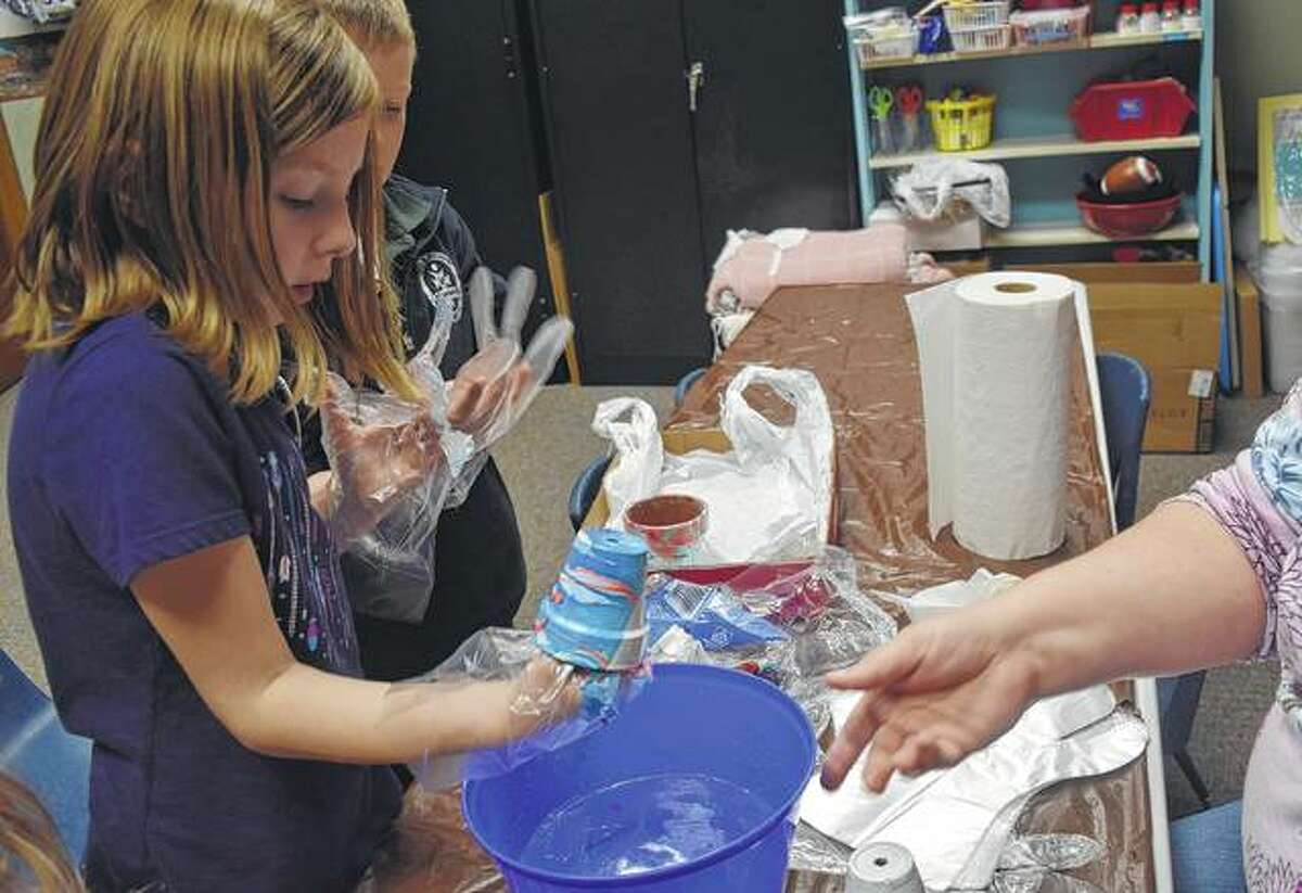 Greta Peterson, 7, the daughter of James and Adrienne Peterson, decorates a flower pot Friday with water and fingernail polish at Jacksonville Public Library. The pots were adorned by filling a bucket with water, using the polish to create designs on top of the water, and dipping the pots into the water, catching the polish along the way.