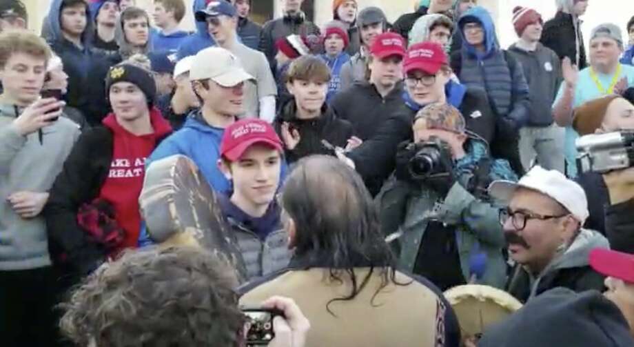 In this Friday, Jan. 18, 2019 image made from video provided by the Survival Media Agency, a teenager wearing a "Make America Great Again" hat, center left, stands in front of an elderly Native American singing and playing a drum in Washington. The Roman Catholic Diocese of Covington in Kentucky is looking into this and other videos that show youths, possibly from the diocese's all-male Covington Catholic High School, mocking Native Americans at a rally in Washington. (Survival Media Agency via AP) Photo: Survival Media Agency / Associated Press