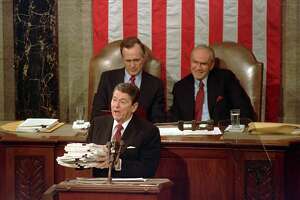 FILE - This Jan. 25, 1988 file photo shows President Ronald Reagan holding up 14-pound continuing resolution for the budget, part of a total package weighing 43-pounds, which the president said was two months late from Congress, during his State of the Union address on Capitol Hill in Washington.  Vice President George H.W. Bush, left, and House Speaker James Wright of Texas listen behind him.  (AP Photo/Bob Daugherty, File)